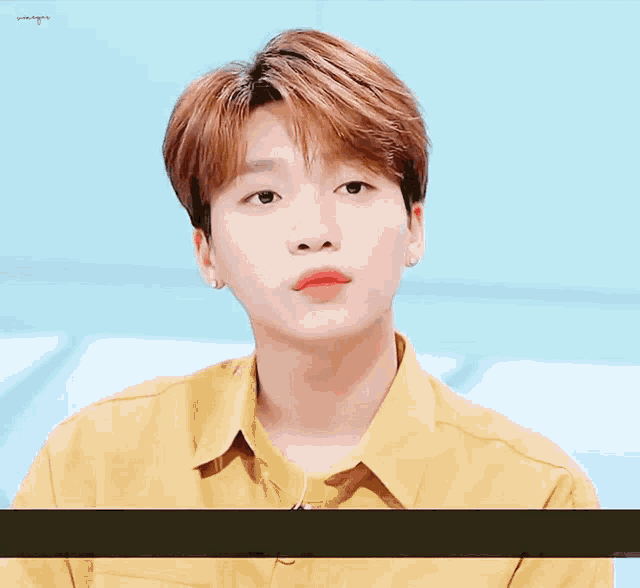 a young man wearing a yellow shirt is looking at the camera with a blue background