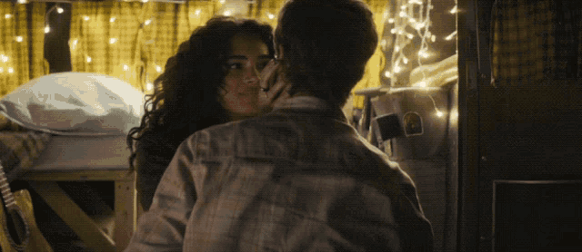 a man and a woman are kissing in a room with christmas lights hanging on the wall