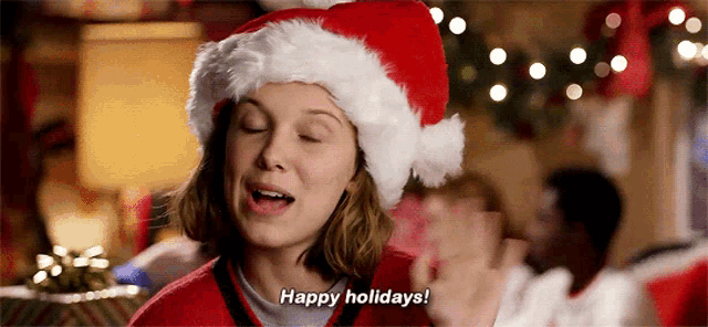 a girl wearing a santa hat is saying `` happy holidays '' .