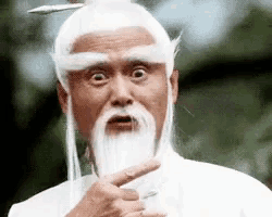 a man with a beard and white hair is pointing at the camera .