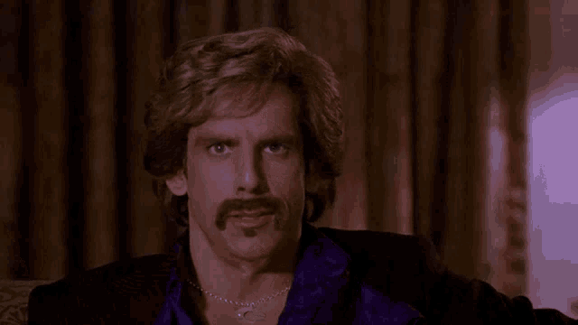 a man with a mustache and a necklace is giving a thumbs up