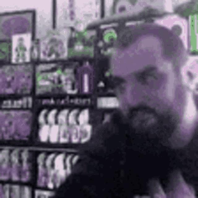 a man with a beard is talking into a microphone in front of a shelf with comics on it .