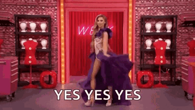 a woman in a purple dress is dancing on a stage with the words `` yes yes yes '' behind her .