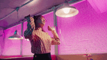 a woman is standing in front of a window with blinds and a lamp .