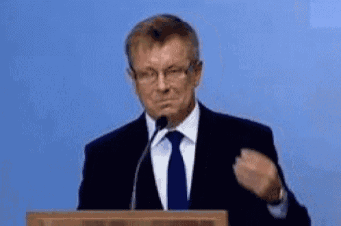 a man in a suit and tie is giving a speech at a podium and making a fist gesture .
