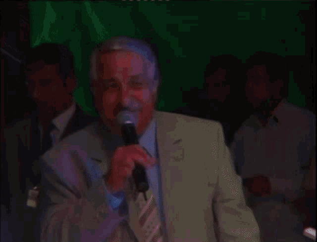 a man in a suit and tie is holding a microphone in front of a green screen