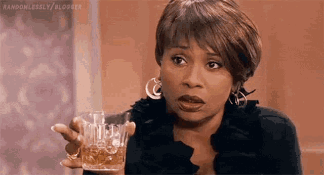 a woman is holding a glass of whiskey in her hand and making a funny face .