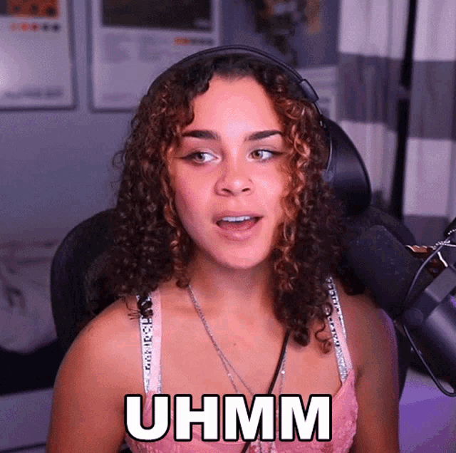 a woman wearing headphones and a pink bra says uhmm in front of a microphone