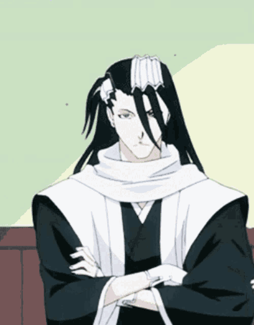 a man with long black hair and a white scarf around his neck stands with his arms crossed