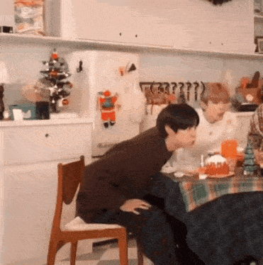 a man is sitting at a table in a kitchen with a christmas tree on the refrigerator .
