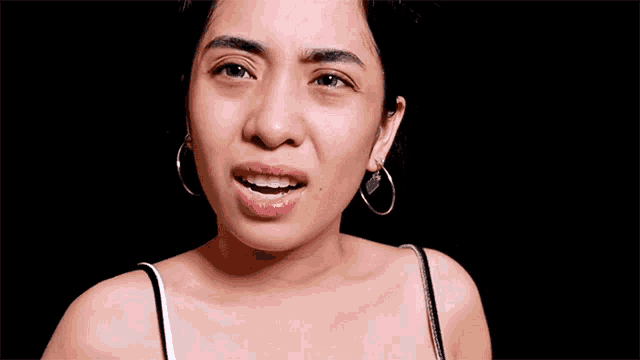 a woman wearing hoop earrings is smiling and making a funny face