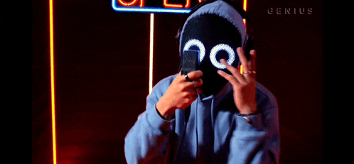 a person wearing a mask and headphones is holding a cell phone in front of a sign that says genius