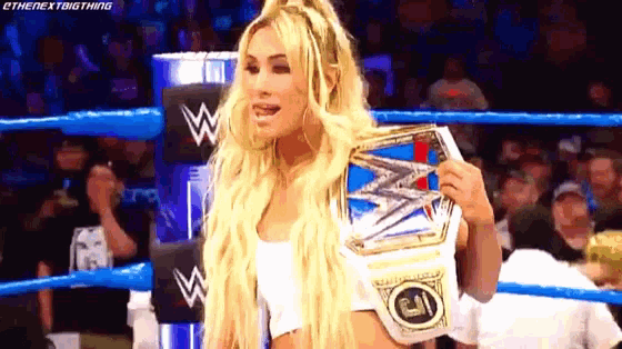 a blonde woman is standing in a wrestling ring holding a championship belt .