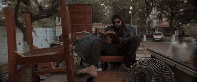 a man reading a book while sitting on a pile of furniture