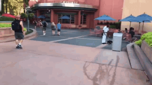 a group of people walking in front of a building with umbrellas .