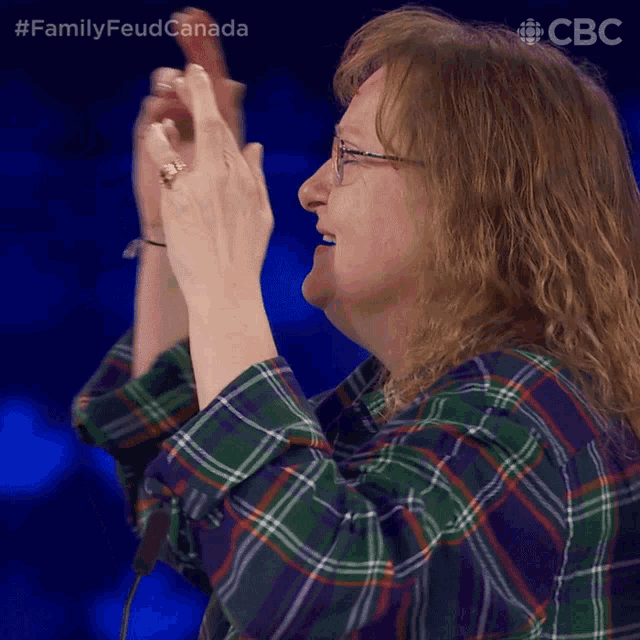 a woman in a plaid shirt is applauding with the hashtag familyfeudcanada