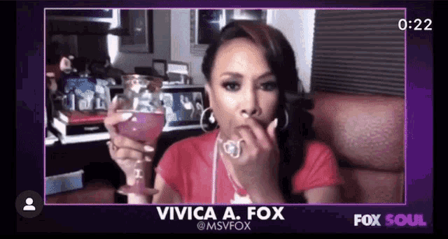 a woman in a red shirt is holding a glass of wine and talking on fox soul