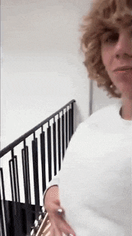a woman with curly hair is standing next to a black railing holding a guitar .