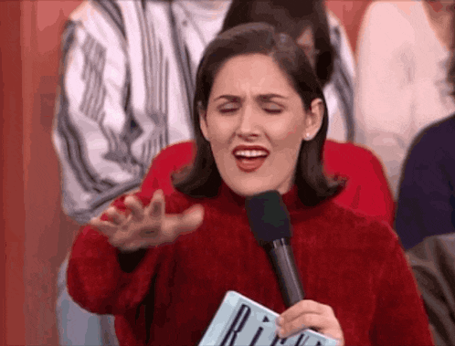 a woman in a red sweater is holding a microphone and a sign that says ri