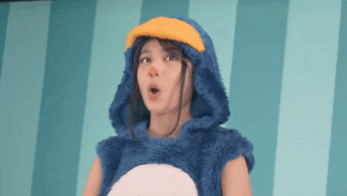 a woman in a blue penguin costume is standing in front of a blue striped wall .