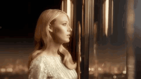 a woman in a white dress is looking out a window .