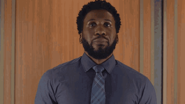 a man with a beard wearing a blue shirt and tie is giving a peace sign