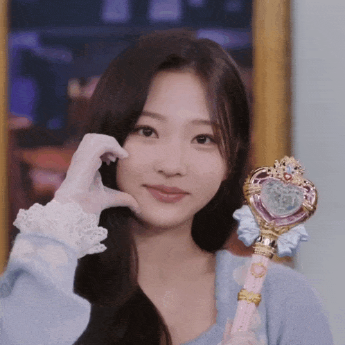 a woman in a blue sweater and white gloves is holding a magic wand and smiling .