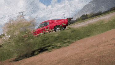 a red car is driving down a dirt road with a mountain in the background