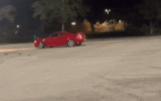 a red car is doing a trick on a dirt road at night .