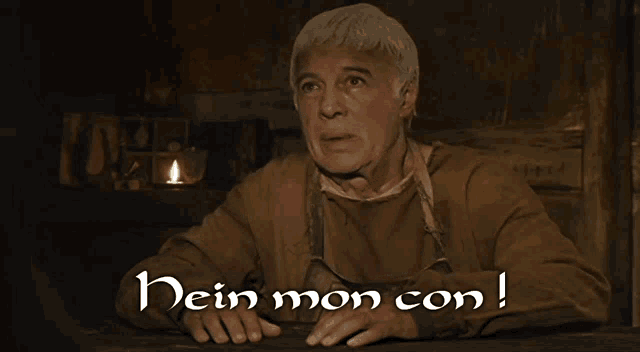 a man sitting at a table with the words " dein mon con " on the bottom right