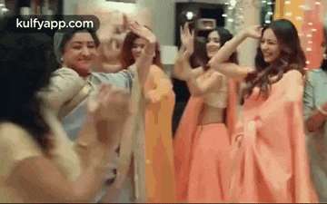 a group of women are dancing together in a room while wearing saris .