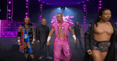 a group of men are walking on a stage and one of them is wearing a pink outfit