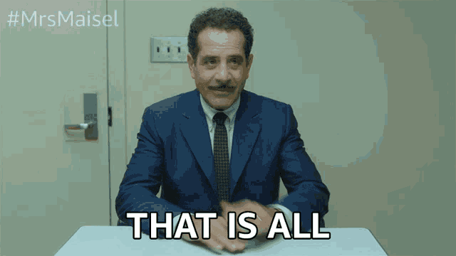 a man in a suit and tie is sitting at a desk and says that is all