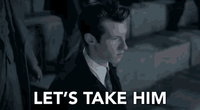 a man in a suit and tie is sitting down with the words `` let 's take him '' written above him .