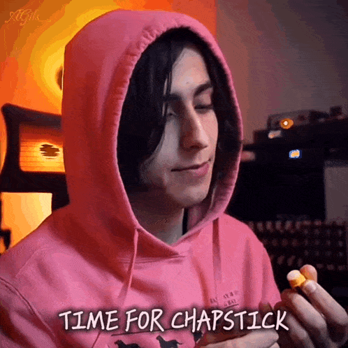a man wearing a pink hoodie is holding a lip balm and says time for chapstick