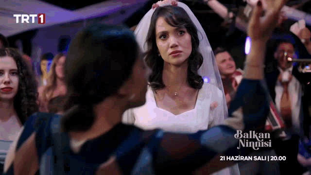 a woman in a wedding dress stands in front of a crowd with trt1 on the bottom right