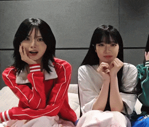 two girls are sitting next to each other with their hands on their faces