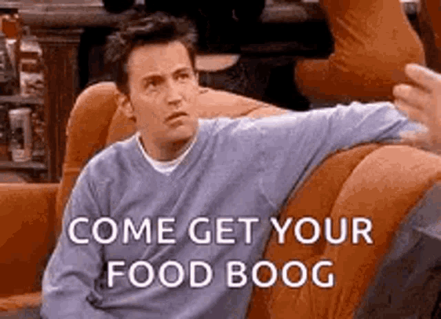 a man is sitting on a couch with his arm outstretched and a sign that says `` come get your food boog '' .