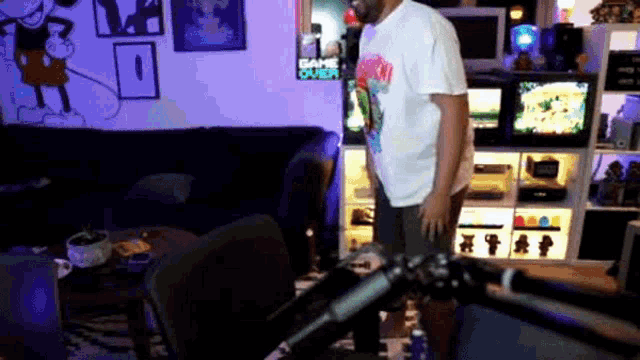 a man is standing in front of a microphone in a living room with a game over sign on the wall