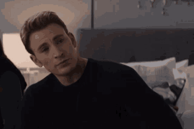 a man in a black sweater is sitting in a bedroom