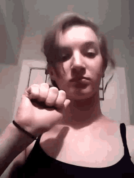 a woman in a black tank top is holding her fist up .