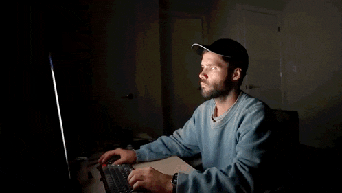 a man with a beard is sitting at a desk using a computer .