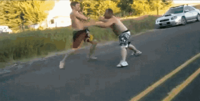two men are fighting on the side of a road
