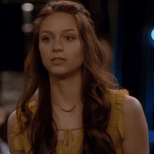 a woman with long red hair wearing a yellow top and a necklace