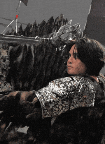 a man in a silver shirt is laying down in front of a statue