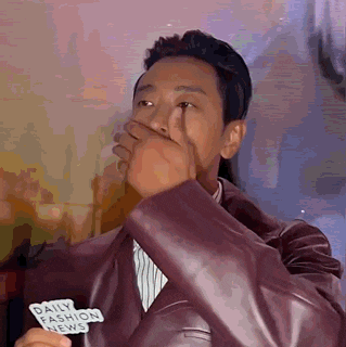 a man wearing a leather jacket is covering his mouth with his hand .