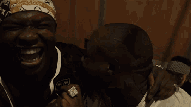 a man wearing a bandana is laughing with another man in a white shirt