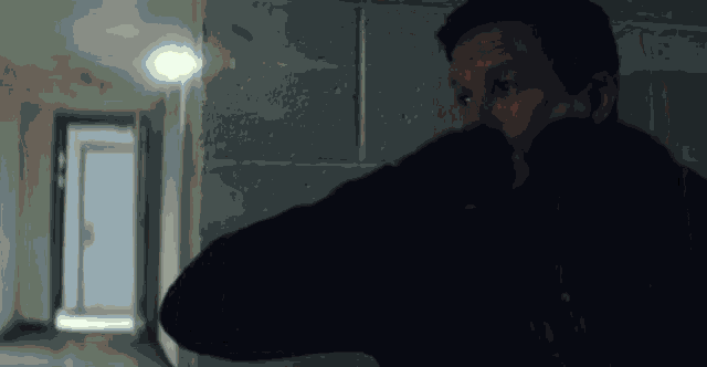 a man in a black jacket is standing in a hallway .