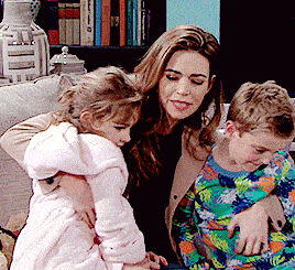 a woman sits on a couch holding two children