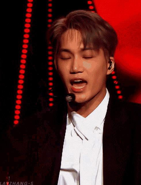 a man in a suit is singing into a microphone with his eyes closed